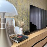 détail d'un meuble de télévision avec lampe moderne, tapisserie feuillue et télévision écran plat