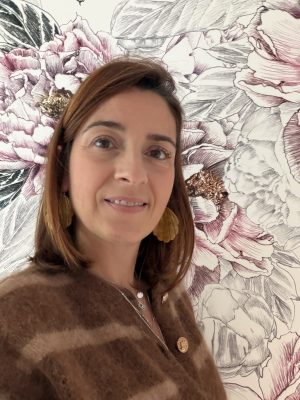photo d'une jeune femme souriante posant devant un pan de tapisserie aux motifs floraux